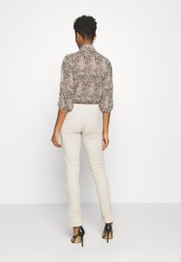 Blouse met luipaardprint en pofmouwen, gecombineerd met beige, aansluitende broek en zwarte hoge hakken, gezien vanuit de rug.