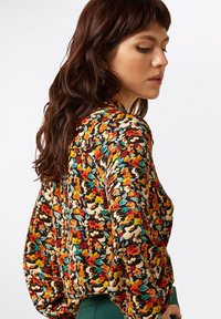 Long-sleeve blouse with a floral pattern in red, yellow, blue, and white on a black background. Features a relaxed fit and soft fabric.