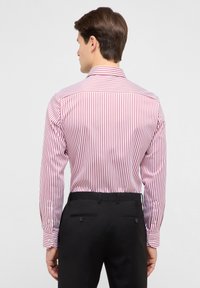 Camicia da uomo a maniche lunghe con sottili righe verticali rosse e bianche, collo classico e polsini con bottoni, abbinata a pantaloni neri.
