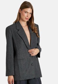Grijze textuur blazer met notch-lapel, dubbele knoopsluiting en lange mouwen. De stof heeft een subtiel patroon en een relaxte pasvorm.