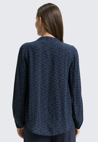 Navy long-sleeve blouse featuring a subtle wavy pattern in light blue and a round neckline. Fabric appears smooth with a relaxed fit.
