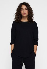 Schwarzes Langarmshirt mit lockerem Schnitt, abgerundetem Saum und weitem Ausschnitt. Weiche Textur und leicht lockere Ärmel.