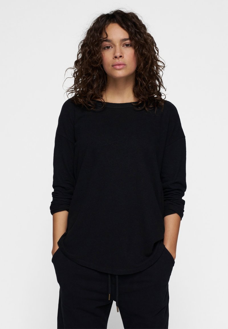 Schwarzes Langarmshirt mit lockerem Schnitt, abgerundetem Saum und weitem Ausschnitt. Weiche Textur und leicht lockere Ärmel.
