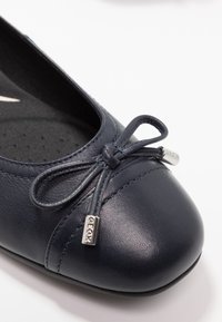 Bailarinas de piel en color navy con punta redondeada, lazo decorativo, acentos de hardware en plata y una plantilla texturizada con perforaciones.