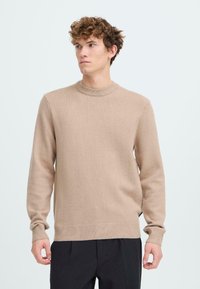 Hellbeige Rundhalspullover aus weichem Material mit gerippten Bündchen und Saum. Der Schnitt ist lässig, gestaltet mit klaren Linien und minimalen Details.