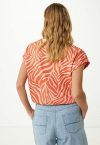 Camiseta de manga corta en naranja con rayas de cebra blancas, con un corte relajado y tejido suave, combinada con unos pantalones de mezclilla azul claro.