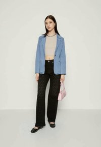 Ανοιχτό μπλε σακάκι πάνω από μπεζ τοπ crop, συνδυασμένο με μαύρο φαρδύ παντελόνι με υφασμάτινη υφή και μαύρες επίπεδες παντόφλες. Κρατά μια ροζ τσάντα.