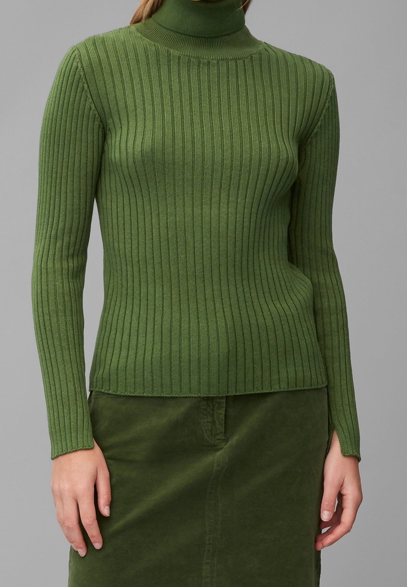 Suéter verde de cuello alto acanalado, hecho de un material suave, con una silueta ajustada, mangas largas y un dobladillo que se alinea con una falda verde a juego.