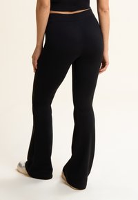 Leggings negras acampanadas hechas de una tela suave y elástica con una cinturilla alta, que presentan una textura suave y sin patrones ni accesorios visibles.