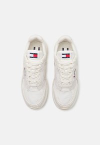 Hvite sportssko laget av mesh og syntetiske materialer, rund tåform, snøring, og Tommy Jeans-logo på tungen.