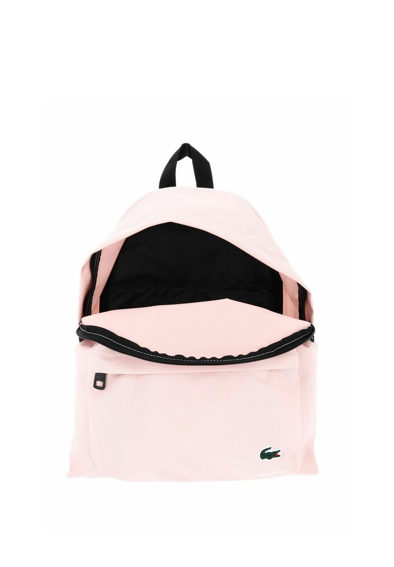Light pink backpack with black interior and zipper, front pocket, black handle, and small green crocodile logo on bottom right.