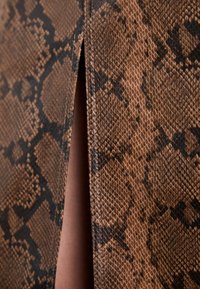 Gros plan sur un tissu marron à texture de peau de serpent avec une fente verticale étroite révélant la peau en dessous.