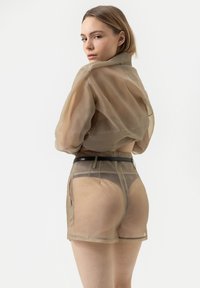 Doorzichtige beige blouse met oversized mouwen, gecombineerd met semi-transparante shorts, voorzien van een zwarte tailleband en subtiele stikdetails.