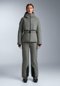 Siva jakna s uzorkom i visokim ovratnikom, s pojasom u struku, i siva hlače koje imaju tamnozelene akcentne boje i teksturiranu tkaninu.