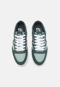 Green and mint canvas sneakers with white laces, perforated accents, and a padded collar. Logo displayed on the tongue. Flat rubber sole.