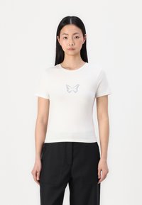 T-shirt en coton blanc à manches courtes et au design ajusté, arborant un élégant graphique de papillon en bleu clair sur la poitrine.
