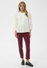 White peplum blouse with embroidered details, complemented by maroon slim-fit pants and black loafers. Smooth fabric and relaxed fit.