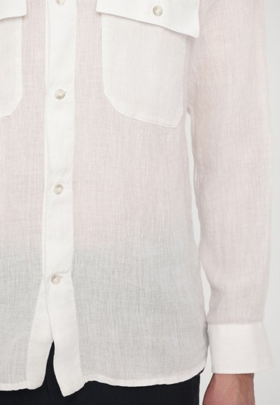 Lightweight, white linen shirt with two chest pockets, buttons down the front, and long sleeves. Soft texture, slightly sheer at the hem.