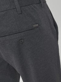 Pantalones de tejido gris con un patrón texturizado, que cuentan con un bolsillo trasero con botón y una pequeña etiqueta metálica de marca en la cintura.