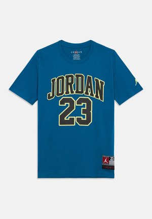 Plava kratka majica s kratkim rukavima s velikim crnim i žutim slovima "JORDAN" i brojem "23" na prednjoj strani, te logotipima Jordan marke na rukavu i rubu.