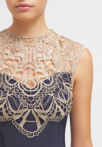 Abito blu marina con intricati ricami dorati al collo e al corpetto, con un design simile al pizzo e una silhouette aderente.