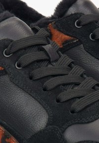 Černé kožené a semišové tenisky mají šněrování, texturovaný design a hnědý zvířecí potisk na boku. Viditelná měkká podšívka.