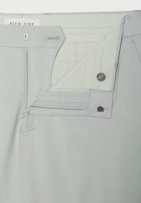 Pantaloni gri deschis cu o textură netedă, având un fermoar și un sistem de închidere cu nasture, cusături contrastante și un eticheta în interior.
