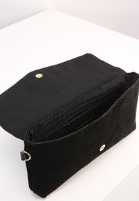 Czarna zamszowa kopertówka z magnetycznym zapięciem, charakteryzująca się gładką teksturą i prostym wzornictwem. Wnętrze zawiera przegrody do organizacji.