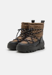 Bottes d'hiver rembourrées marron avec des semelles épaisses noires, des bordures noires et des lacets à motif noir et blanc, le tout sur un fond blanc.