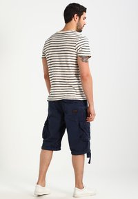 Stripet beige og marineblå t-skjorte sammen med marineblå cargo-shorts, med sidelommer, rullet kant og et tekstilmerke på baksiden.