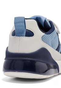 Blå och vit sneaker med ett meshtyg på ovansidan, vadderad krage, dragflik och en kurvad, glänsande marinblå sula. Texturerad yta med sömnadsdetaljer.