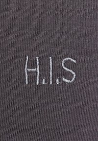 Grau gemusterter Stoff mit feiner Rippenstruktur und gestickten Buchstaben "H.I.S" in silberner Faden. Keine zusätzlichen Muster oder Akzente vorhanden.