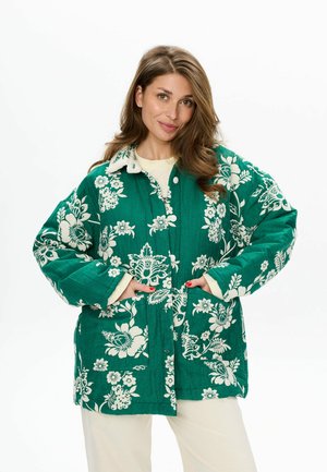 Groene bloemenpatroon jas gemaakt van gestructureerde stof met een knoopsluiting aan de voorkant, grote zakken en een contrasterende witte kraag.