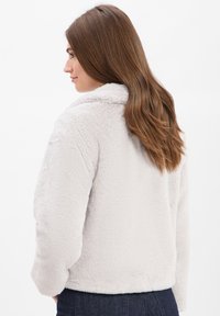 Jasnoszara kurtka z futra sztucznego z kołnierzem, długimi rękawami i miękką teksturą, z luźnym krojem i bez widocznych elementów metalowych.