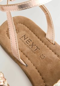 Offene Sandale mit einem weichen beigen Wildlederfußbett, metallisch rose-goldenen Riemen und geprägtem Markenlogo "NEXT Forever Comfort" auf der Innensohle.