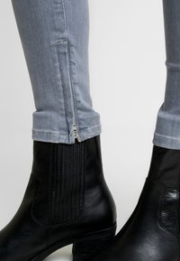 Černé kožené kotníkové boty s texturovanými bočními panely, nošené s světle modrými džínami s rozepínatelným lemem a zúženým střihem.