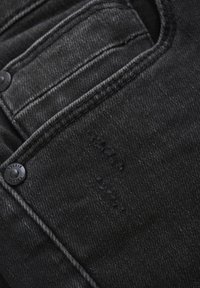 Zwarte denimstof met een onderscheidende textuur, met zichtbare stiksels en knoopdetails op het voorvakgebied.