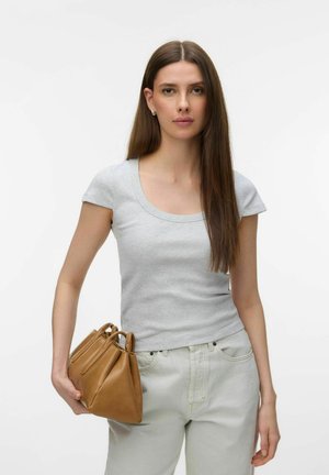 Woman with long brown hair wearing a grey fitted short-sleeve top and light jeans, holding a brown leather handbag in her left hand.
