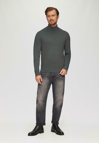Ciemnozielony sweter z golfem, o miękkiej fakturze, dopasowany krój, zestawiony z przetartymi szarymi dżinsami i czarnymi sznurowanymi butami. Prosty, nowoczesny design.