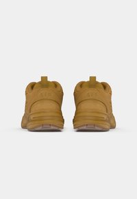 Een paar lichtbruine suede sportschoenen die achterwaarts zijn gericht, met zichtbare gepolsterde hielen en "AIR" branding op elke hieltab.