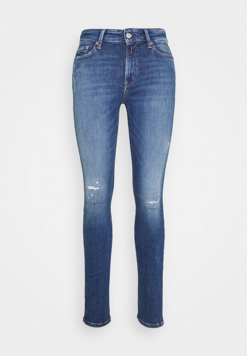 Jeans ajustados de denim azul medio con ligero desvanecimiento y parches desgastados. Cuenta con cierre de botón y cremallera, y diseño de cinco bolsillos.