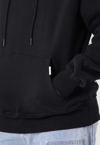 Sudadera negra con cordones, bolsillo delantero y puños acanalados. Material de mezcla de algodón con una textura suave y una pequeña etiqueta lateral.