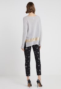 Harmaa neule joka on varustettu kultaisella metallisella raidalla helmassa, yhdistetty mustiin housuihin, joissa on avaruusteemainen printti, ja mustiin korkokenkiin.