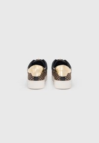 Baskets en cuir noir avec des accents métalliques dorés, des clous dorés texturés à l'arrière et une semelle en caoutchouc blanche.