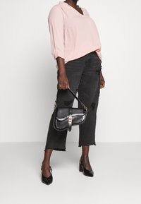 Czarne, krótkie dżinsy z postrzępionym dołem, miękka różowa bluzka i czarna torebka o fakturze z złotymi elementami, w połączeniu z czarnymi szpilkami.