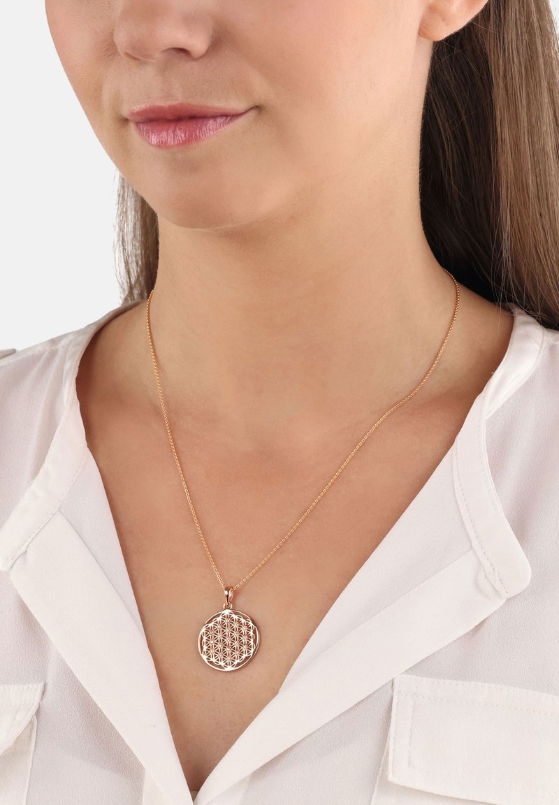 Rund hängsmycke i roseguld metall med ett blommönster. Kedjan är tunn och delikat, vilket kompletterar hängsmyckets design.