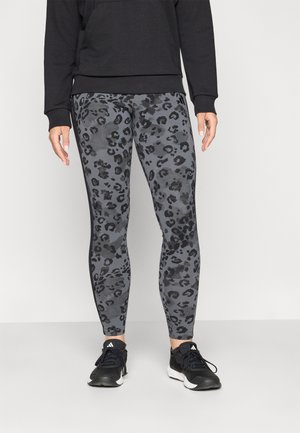 Grå leggings med et svart leopardmønster, laget av elastisk materiale, kombinert med en svart hettegenser og svarte joggesko.