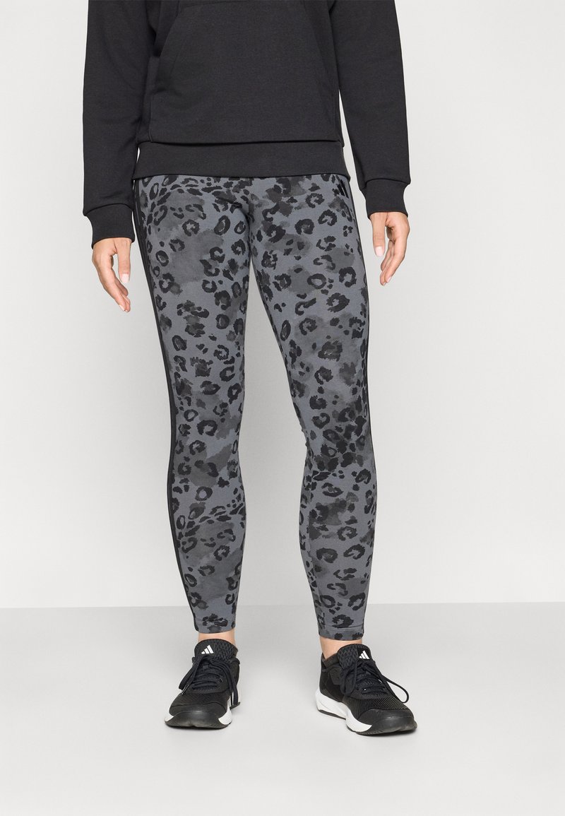 Leggings grigi con un motivo di stampa leopardata nera, realizzati in materiale elasticizzato, abbinati a una felpa nera e scarpe da ginnastica nere.