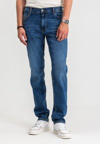 Niebieskie dżinsy z prostą nogawką, pięcioma kieszeniami, widocznym przeszyciem, noszone z białymi trampkami.