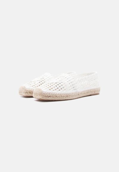 Λευκά υφασμάτινα παπούτσια τύπου slip-on με πλεκτές σόλες από τζούτ, απεικονιζόμενα σε ένα απλό απαλό γκρι φόντο.